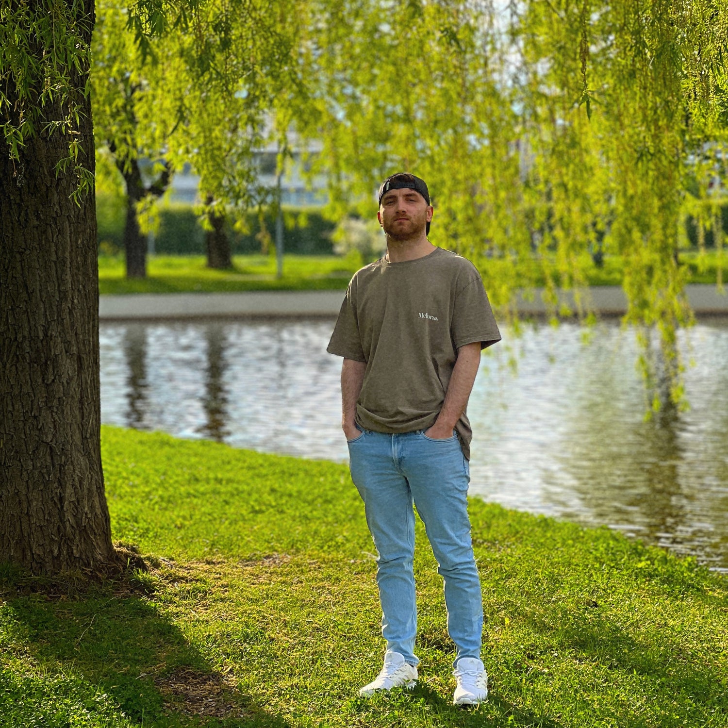 Model trägt das ROUGH CUT Oversized T-Shirt von Melioras in Vintage-Washed-Khaki. Shooting im Park Leipzig unter grüner Trauerweide.